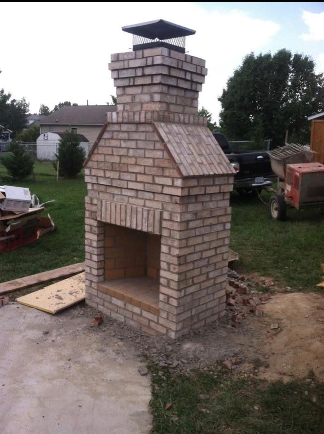 Tall freestanding brick outdoor fireplace with chimney cap