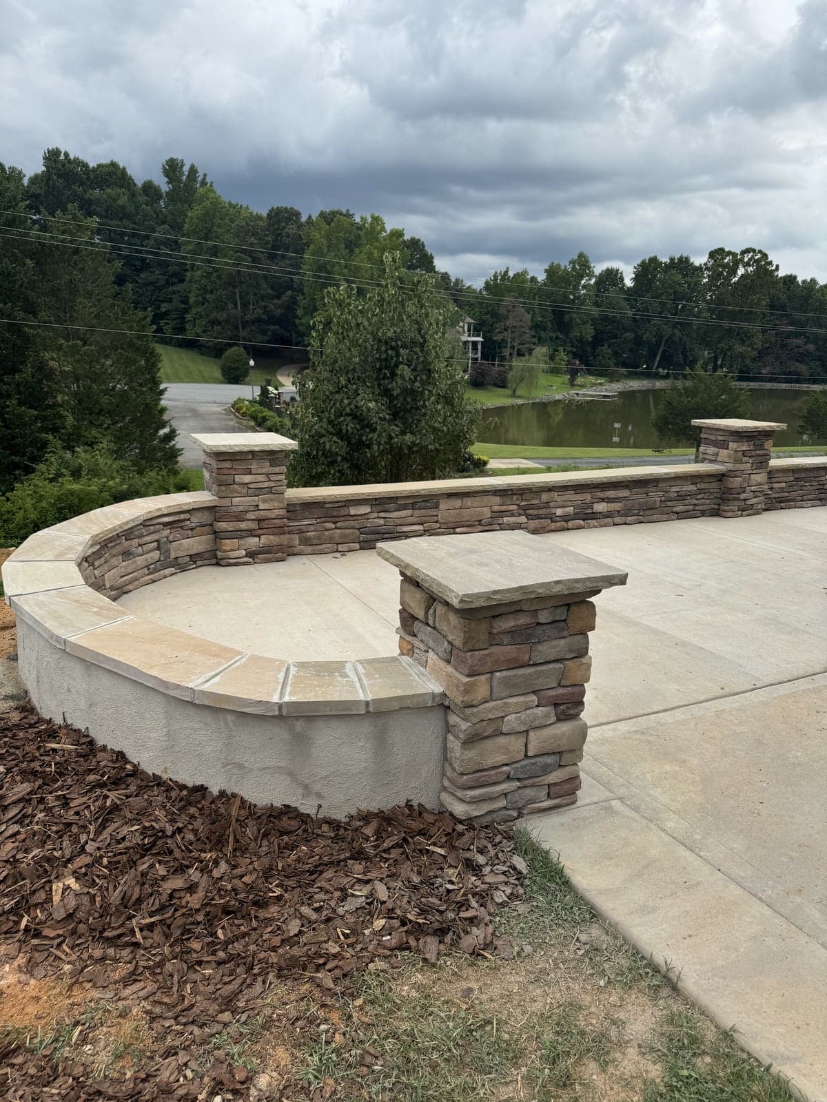 Curved stacked-stone seat wall with stone columns overlooking a lake